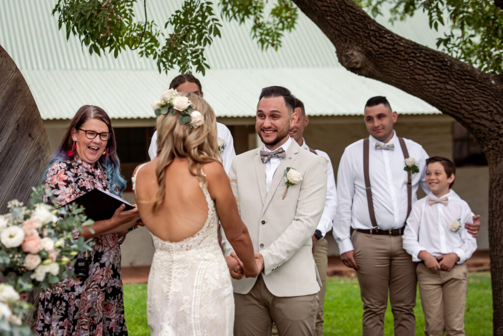 A groom smiling at his bride during an outdoor wedding ceremony
