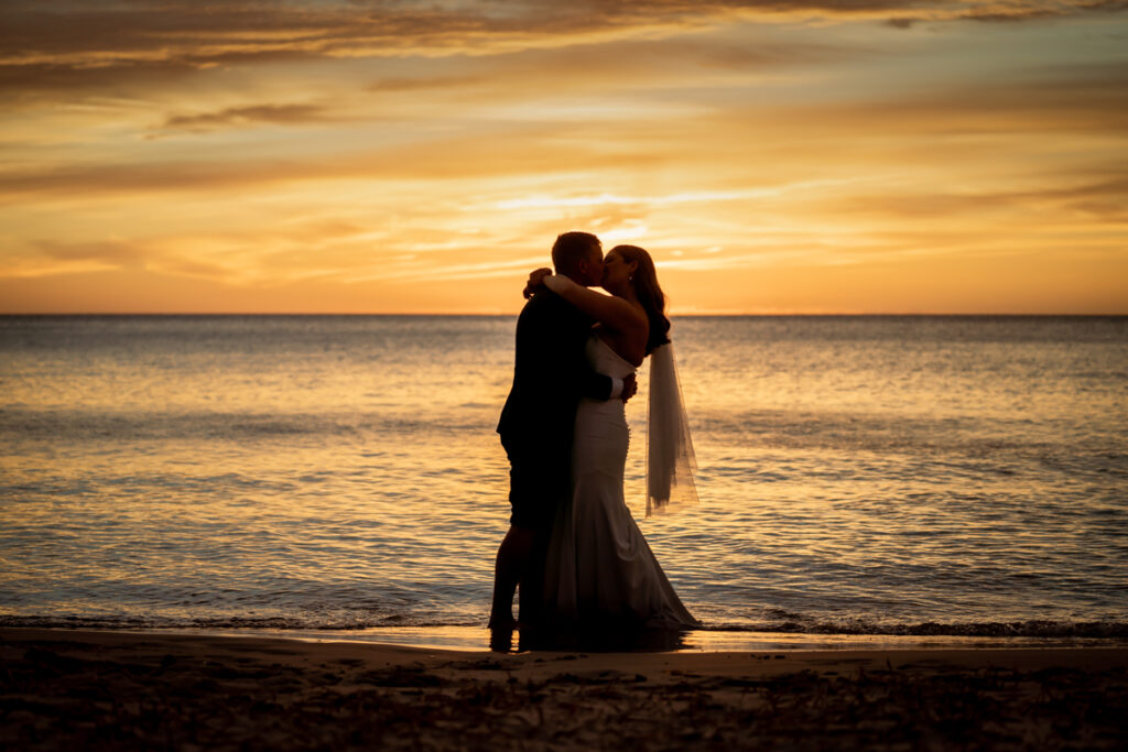 A wedding couple kissing beside the sea at sunset