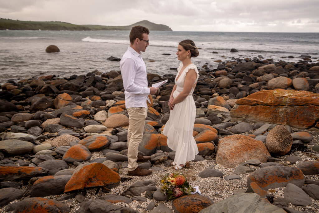 A wedding couple holding hands on a rocky beach
