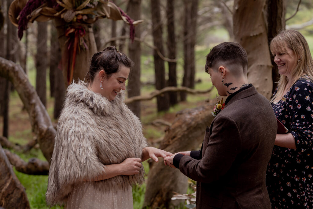 A couple exchanging rings with their celebrant in a forest