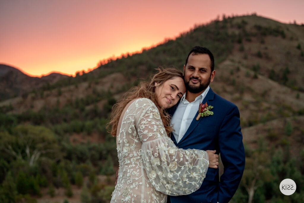 A wedding couple embracing beneath a sunset sky in the ranges