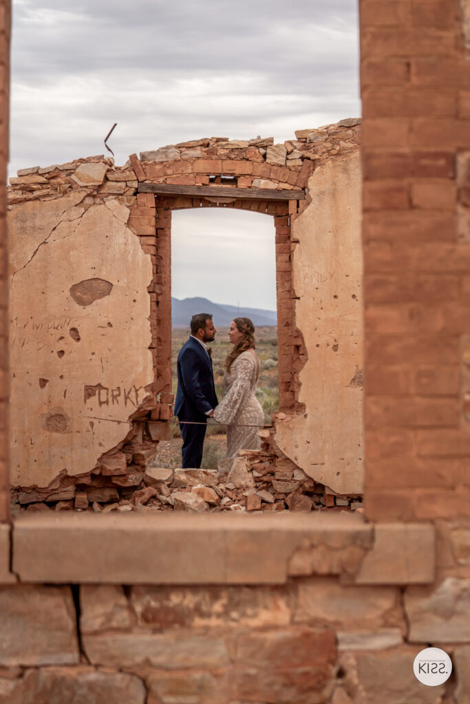 A wedding couple framed by the doorway of a ruined stone building