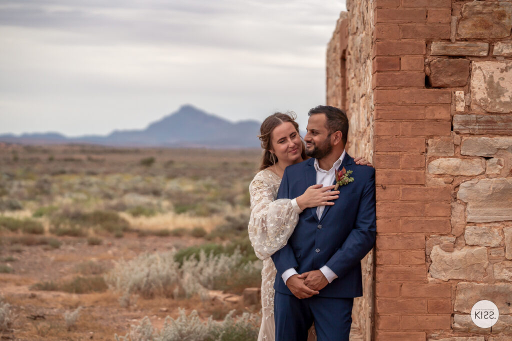 A wedding couple embracing beside a ruined stone wall