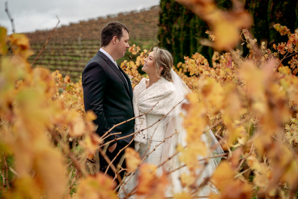 A wedding couple smiling at each other among autumn vines