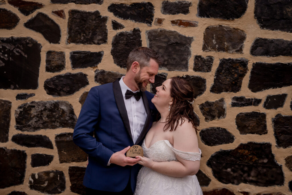 A wedding couple holding hands beside a stone wall