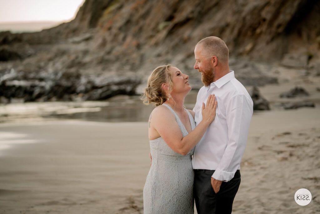 A bride smiling at her groom at the water's edge