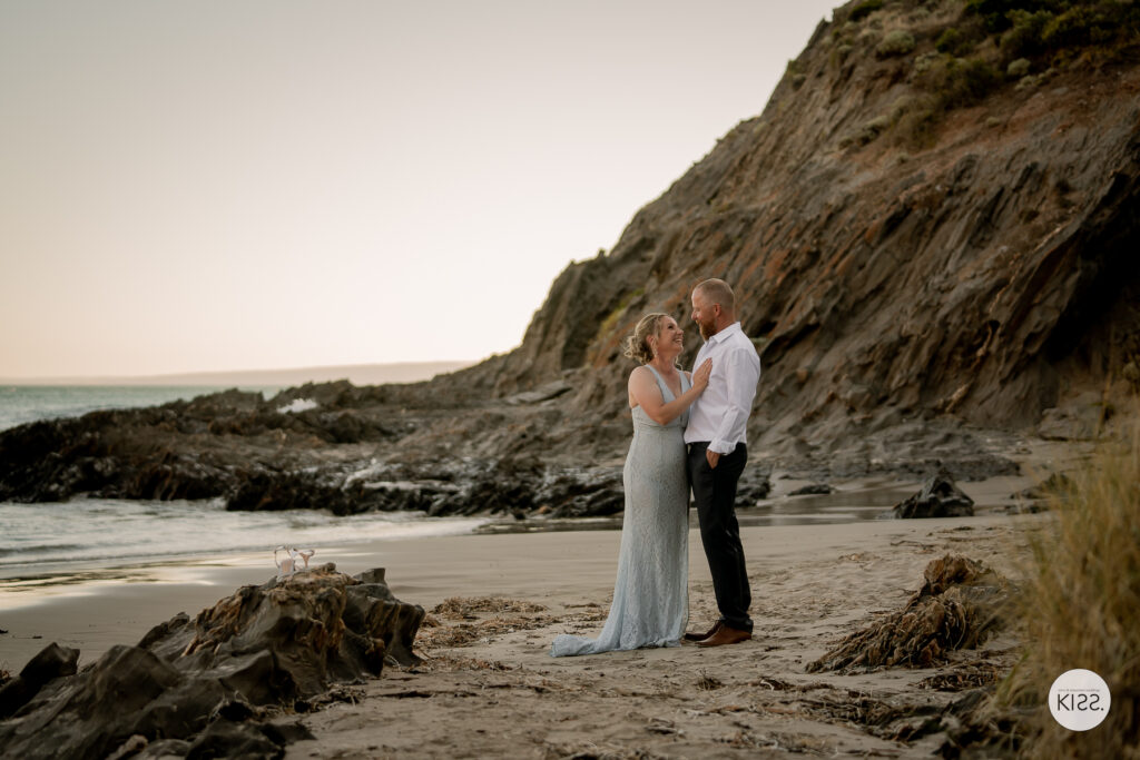 A wedding couple standing together beside a rocky cove