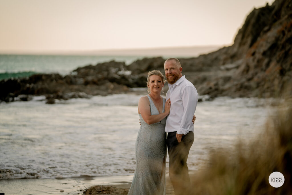 A wedding couple embracing beside a rocky beach