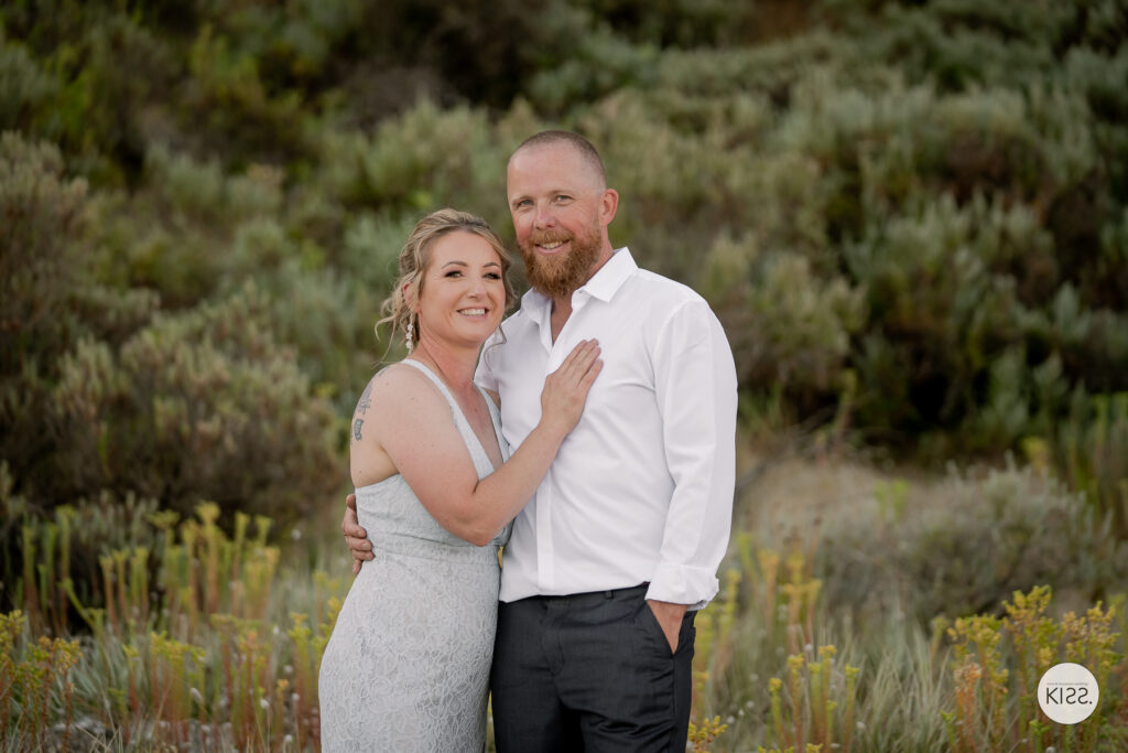 A wedding couple posing together above the beach