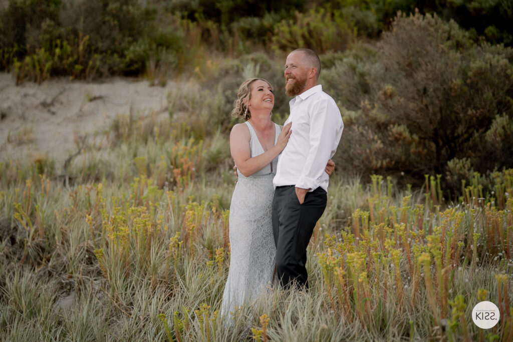 A wedding couple smiling together among coastal plants