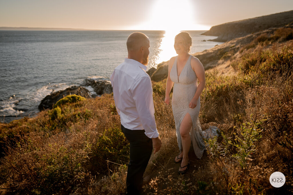 A wedding couple looking at each other above the sea at sunset