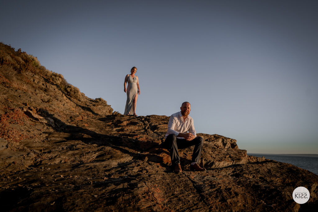 A wedding couple posing on a rocky coastal hillside