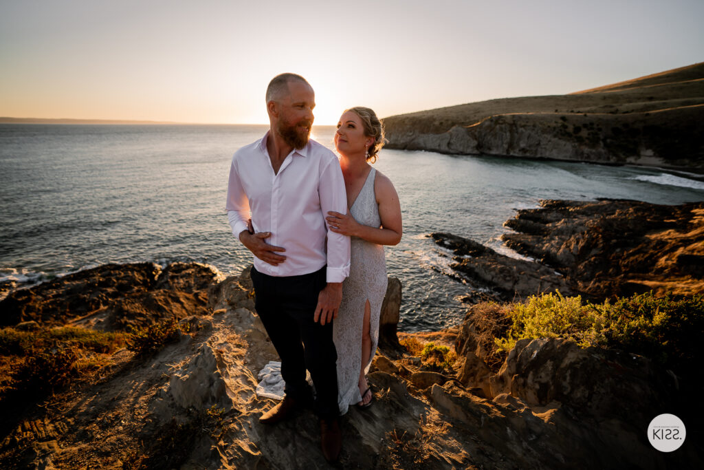 A wedding couple walking across coastal rocks in evening light