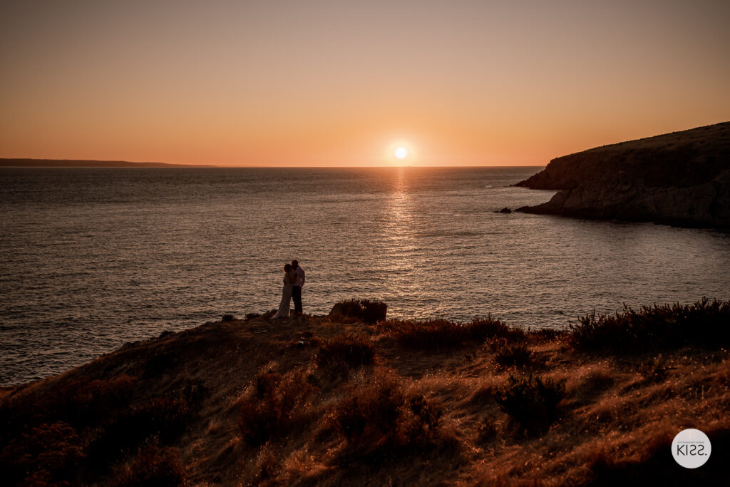 A wide view of a couple beside the ocean at sunset
