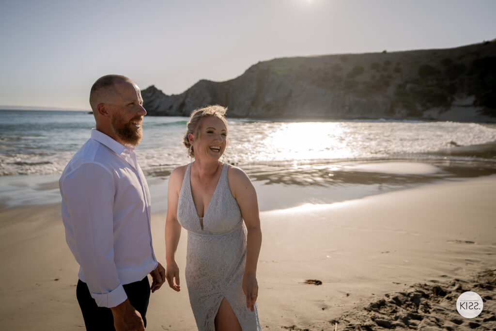 A wedding couple smiling together beside sunlit water