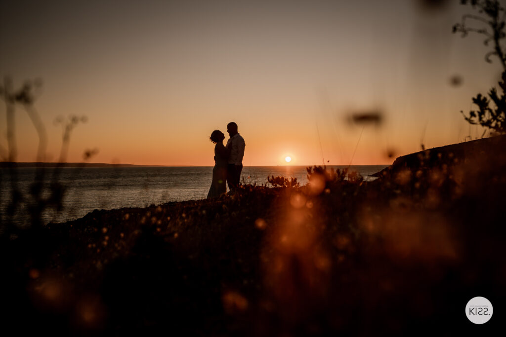 A couple silhouetted against a glowing coastal sunset