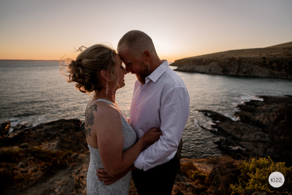 A wedding couple touching foreheads beside the sea at sunset