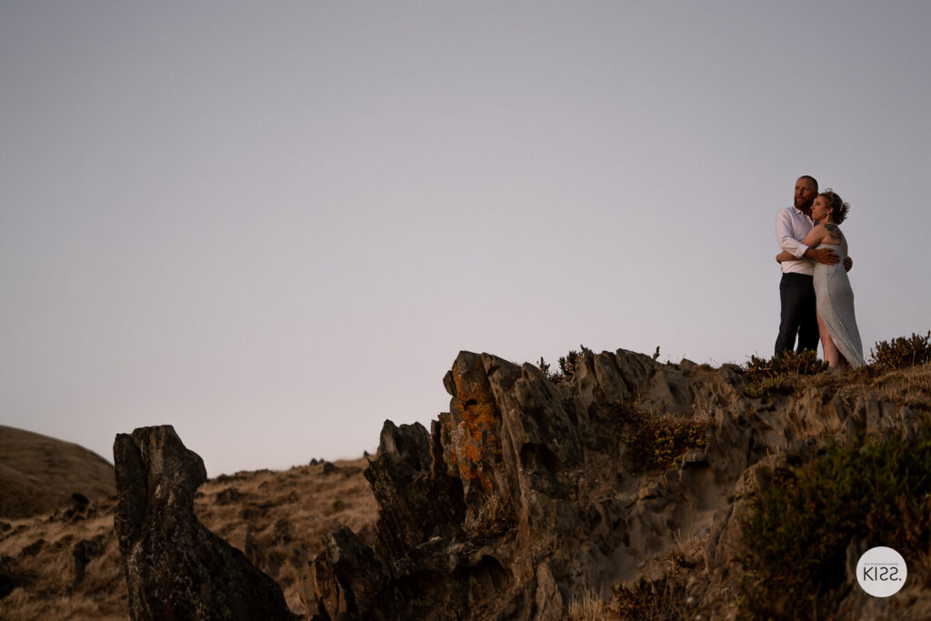 A wedding couple standing together on a rocky headland