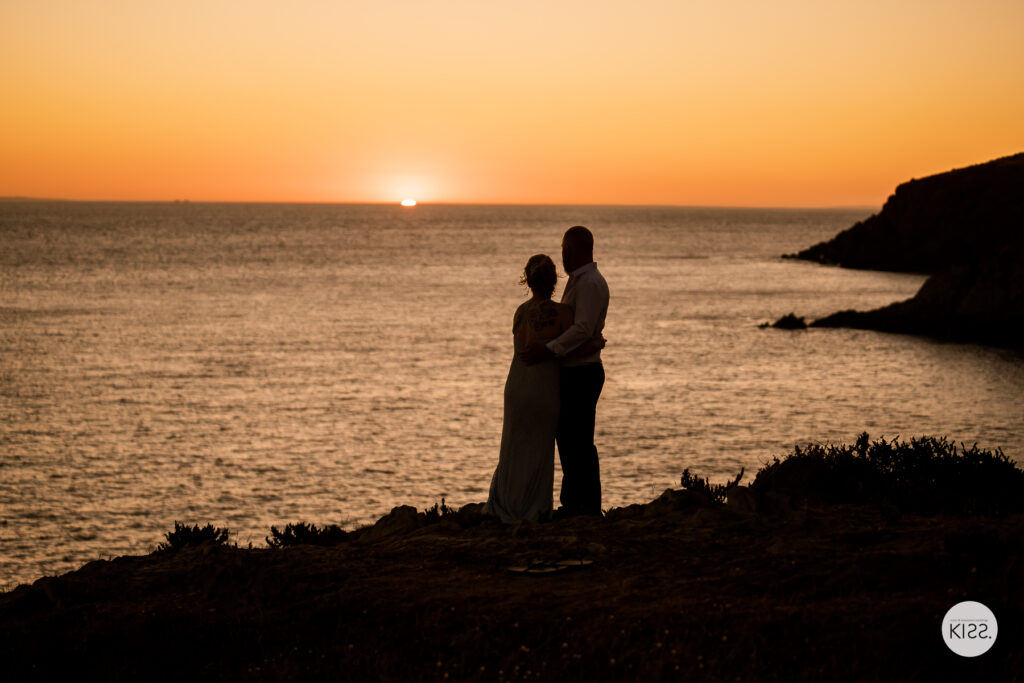 A wedding couple silhouetted beside the ocean at sunset
