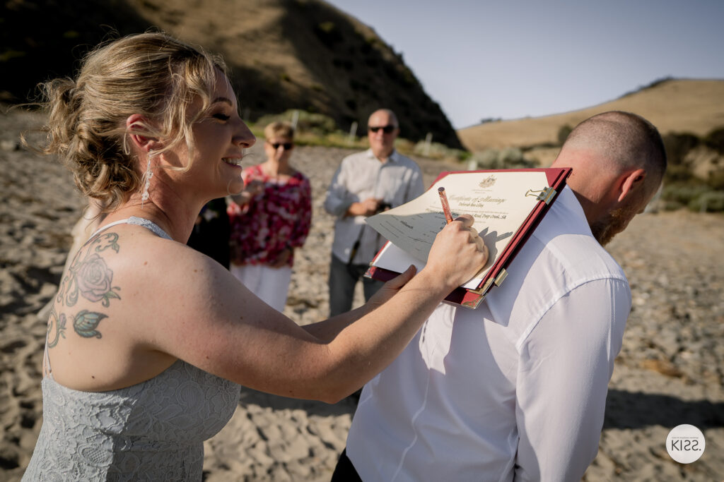 A bride signing the marriage register resting on her groom's back