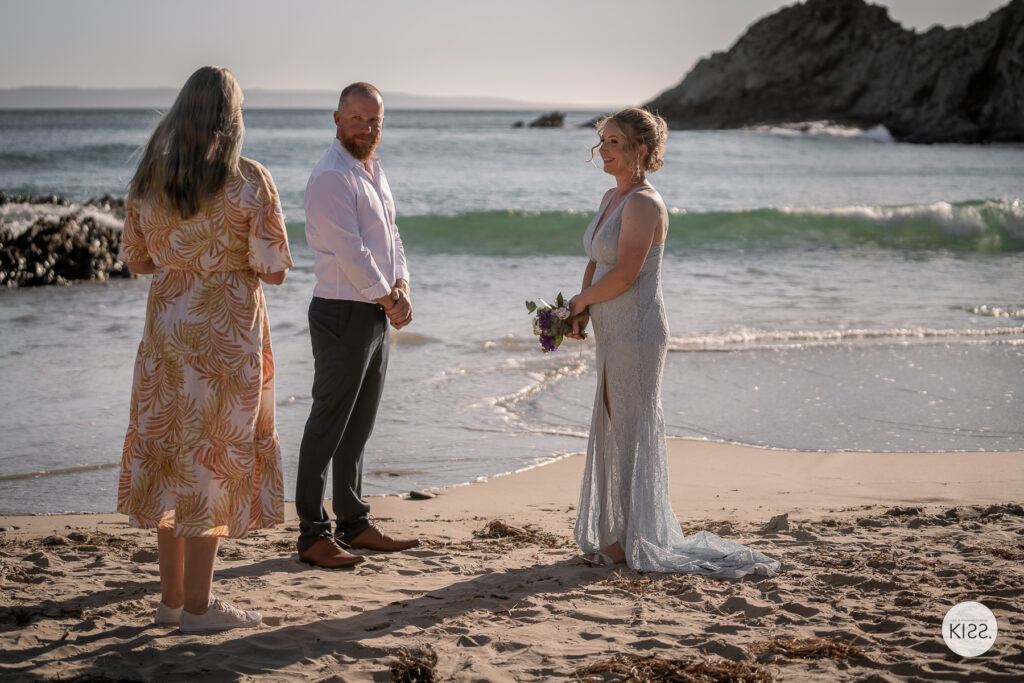 A couple exchanging vows with their celebrant beside the sea