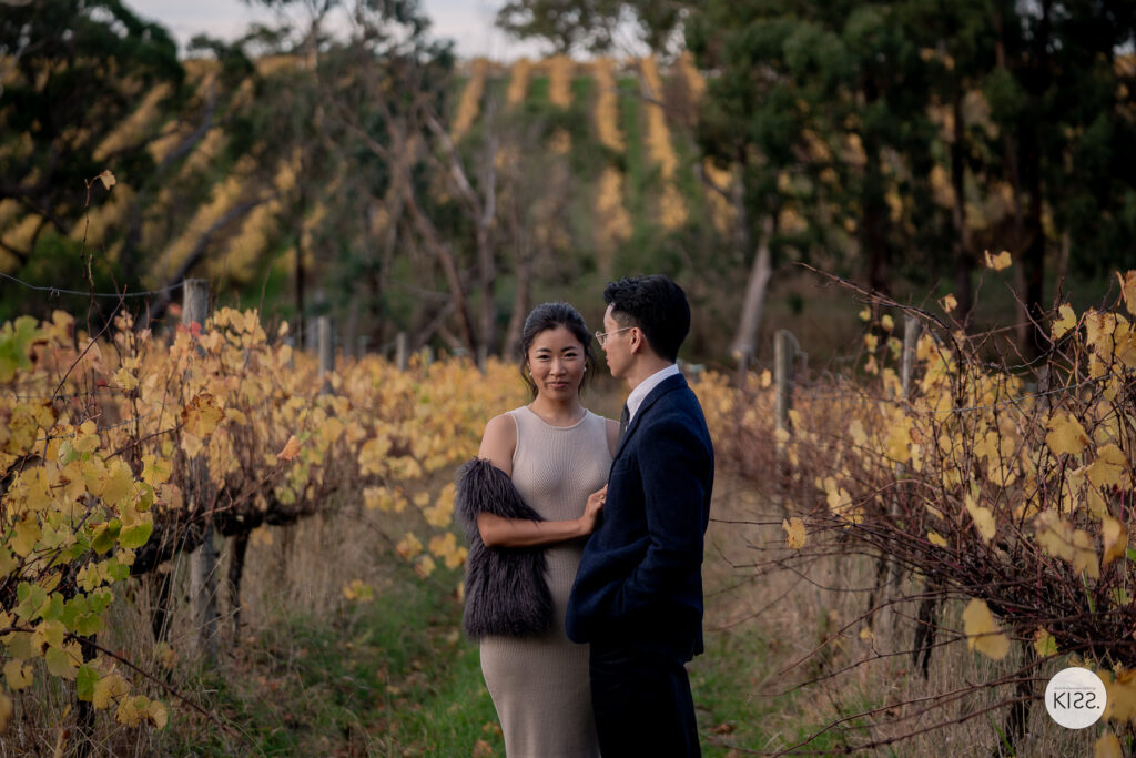 A couple holding hands beside autumn vines