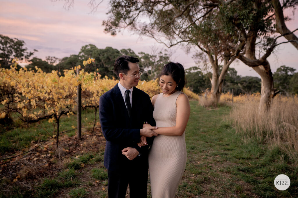 A wedding couple embracing beside autumn vines