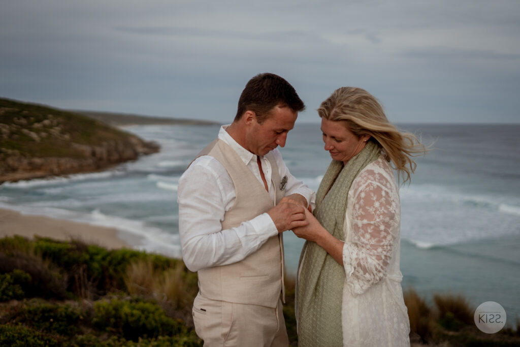 A couple looking at their joined hands above the ocean