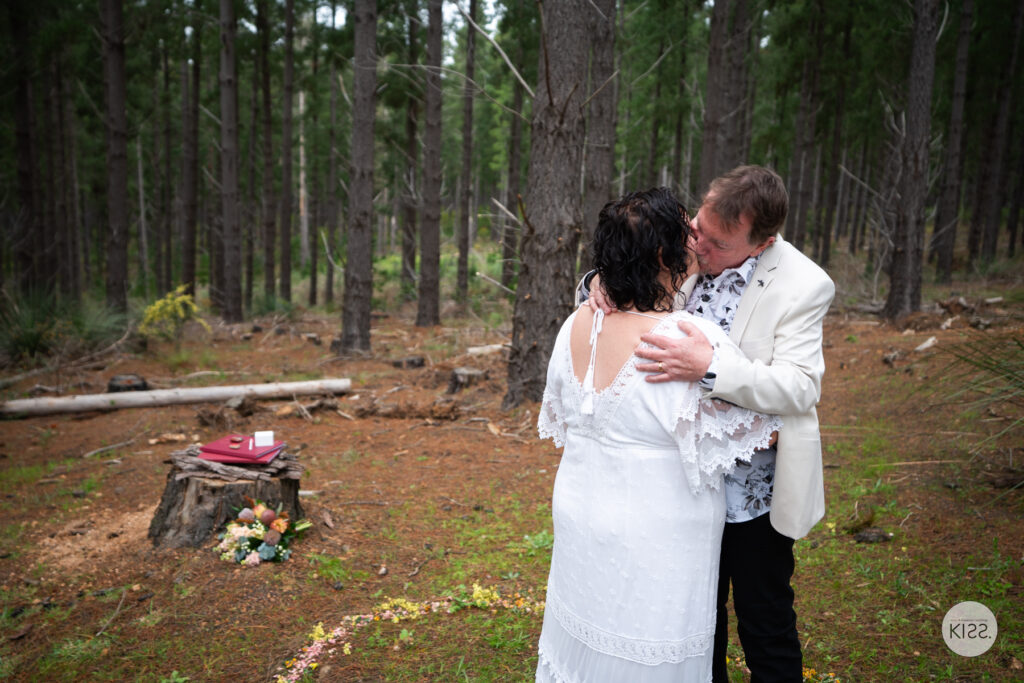 A wedding couple kissing in a forest clearing