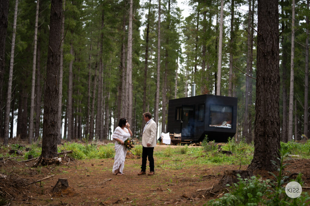 A couple walking away from a tiny cabin among pine trees