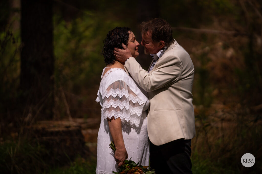 A groom touching his bride's face in the forest