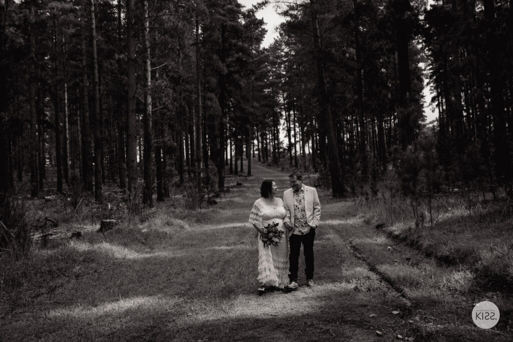 A wedding couple standing on a broad forest path in black and white
