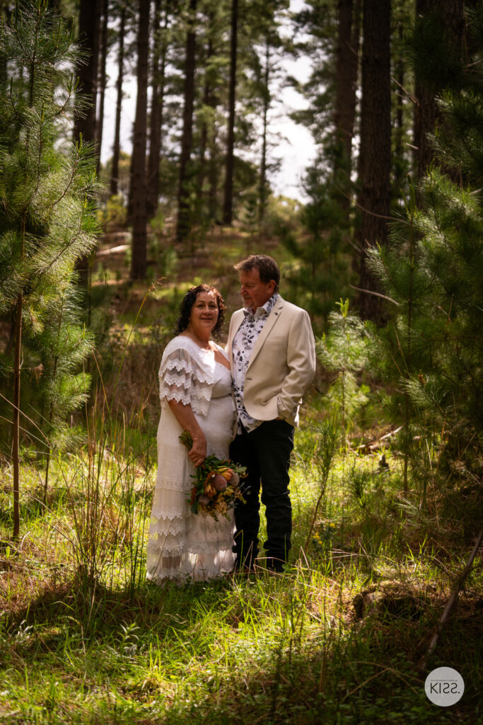 A wedding couple embracing among sunlit pine trees