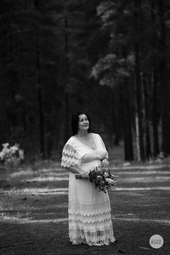 A bride holding her bouquet on a forest path in black and white