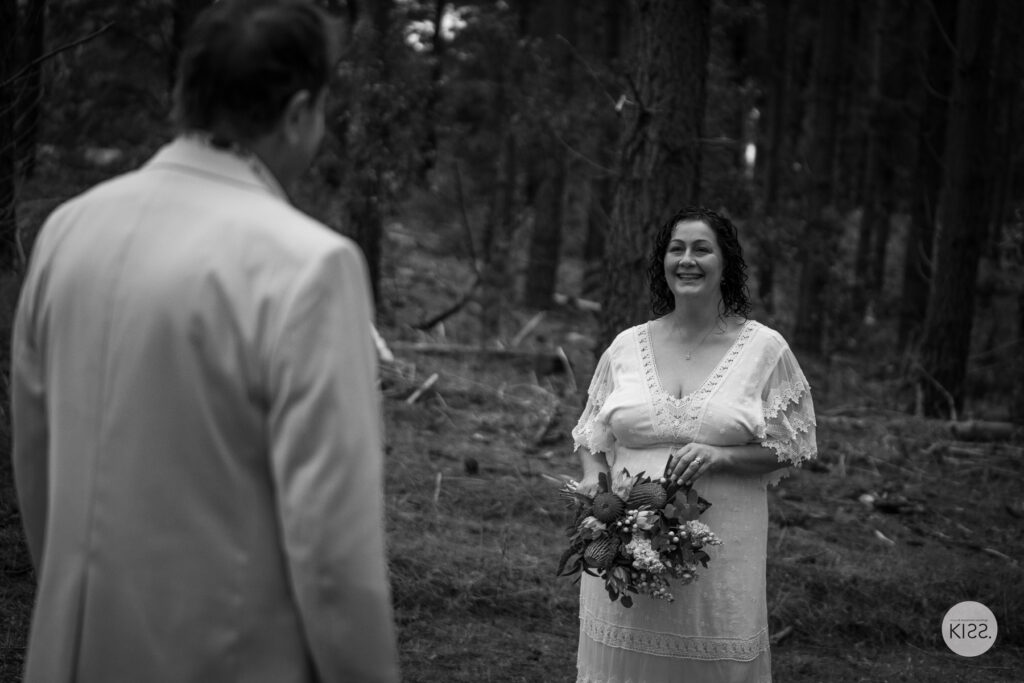 A bride looking towards her groom in a forest in black and white