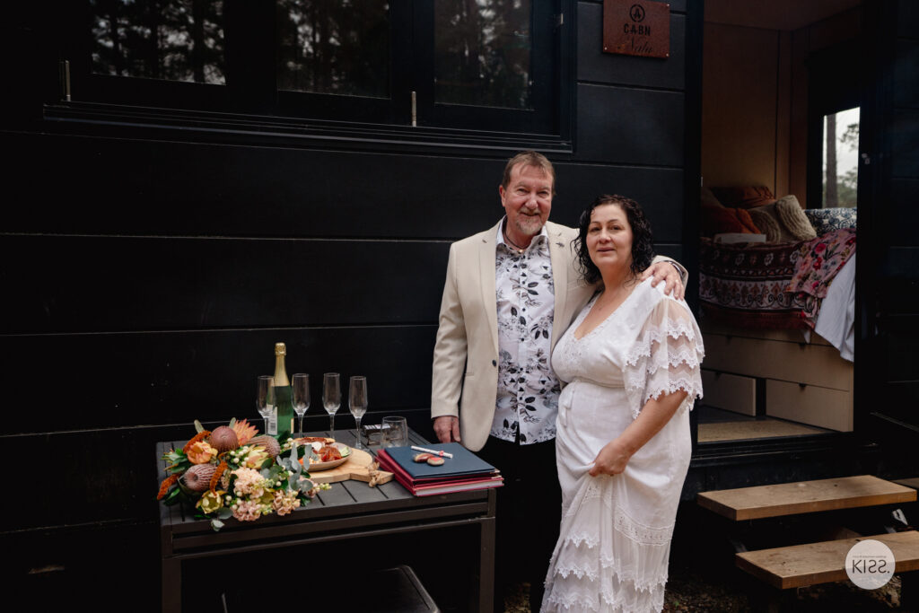 A wedding couple beside a grazing table outside their cabin