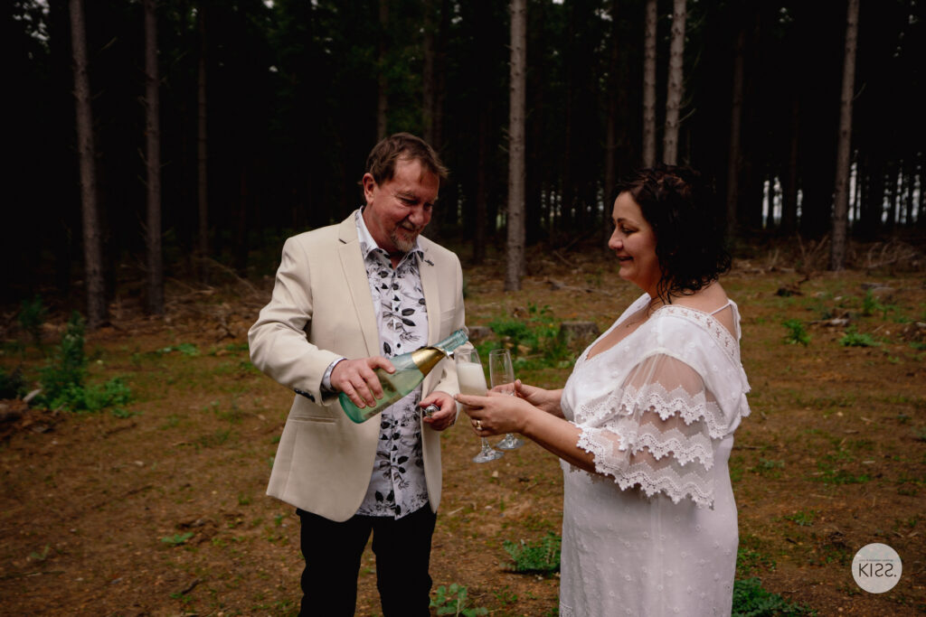 A groom pouring a drink for his bride after their forest wedding