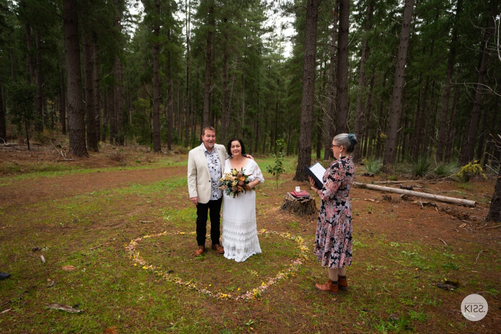 A wedding couple and celebrant together among tall trees