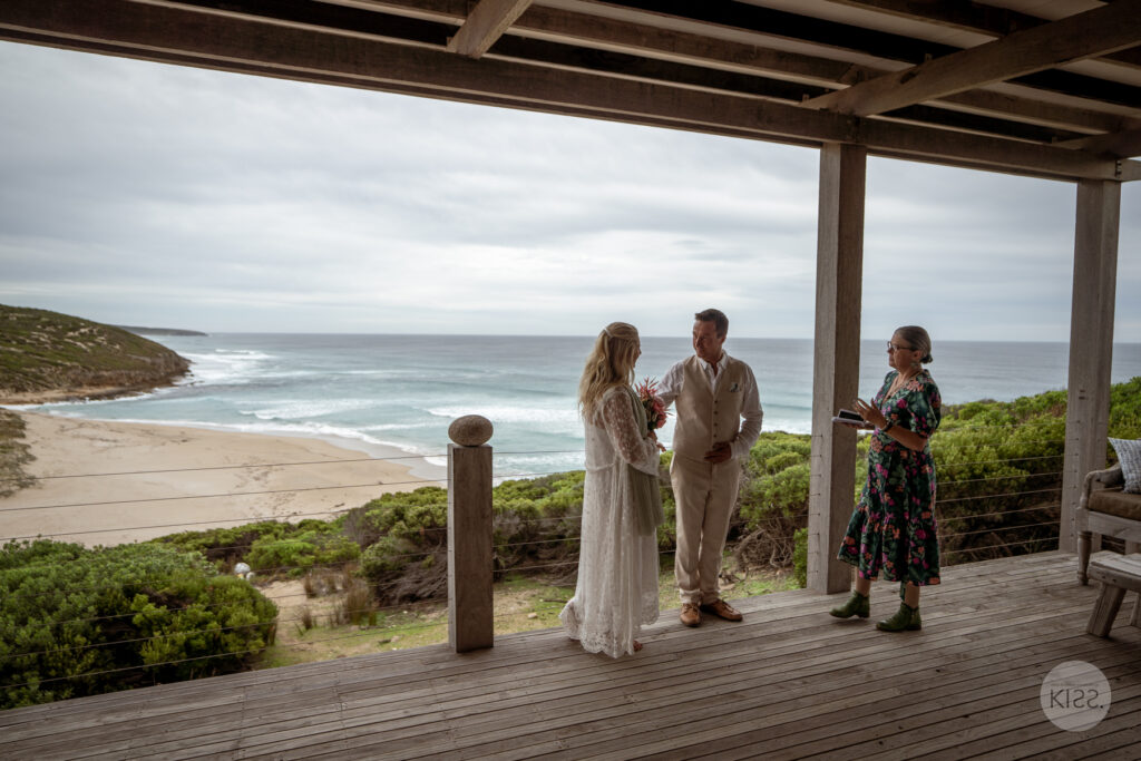 A couple and celebrant beneath a covered ocean-view deck