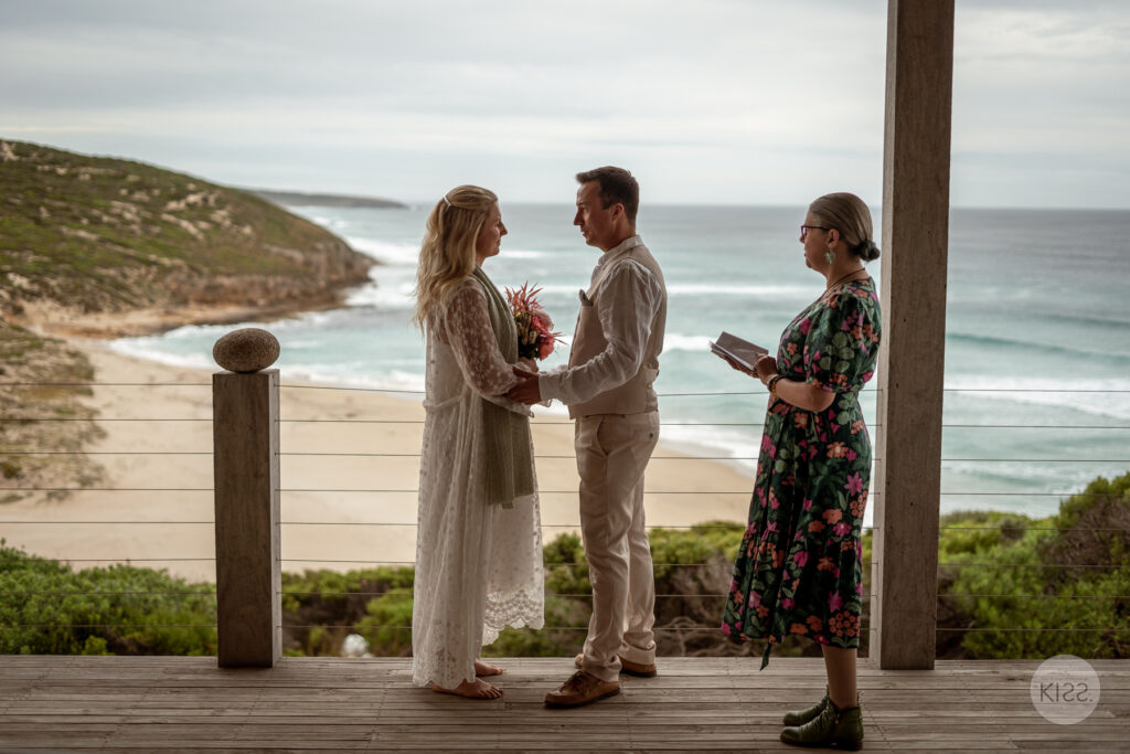 A wedding couple holding hands beside their celebrant