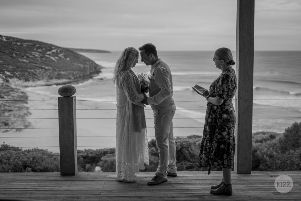 A couple kissing beside their celebrant in black and white