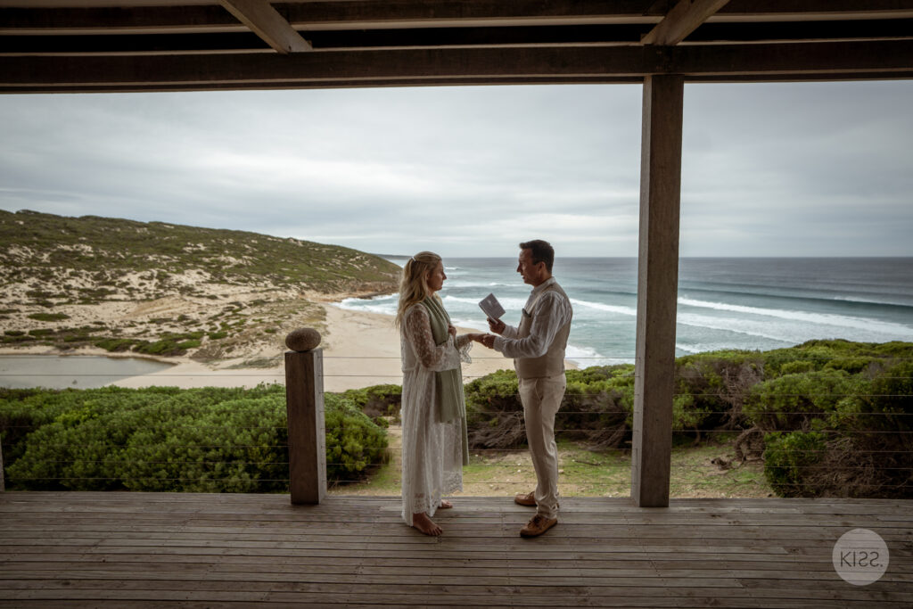 A couple exchanging vows beneath a covered coastal deck