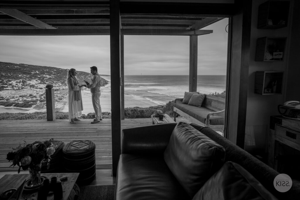 A wedding couple on a coastal deck viewed from indoors in black and white
