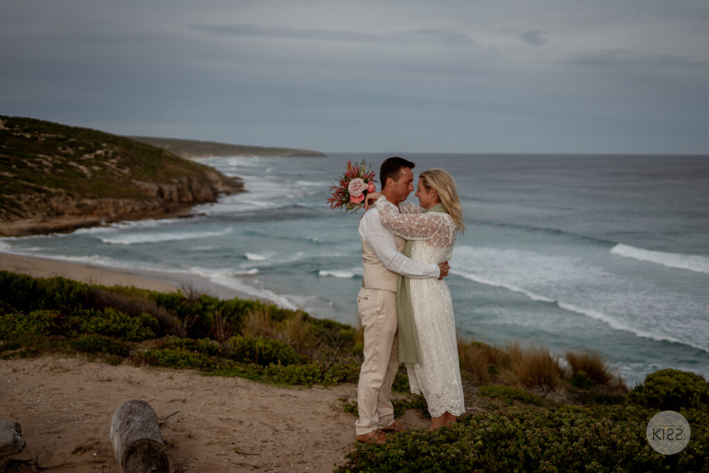 A wedding couple embracing above the ocean