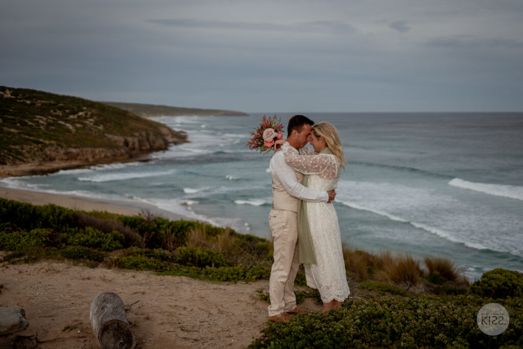 A wedding couple embracing above the ocean