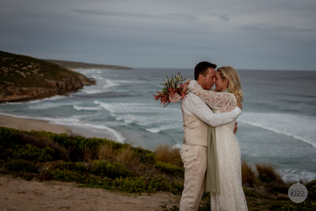 A wedding couple kissing with the coastline behind them
