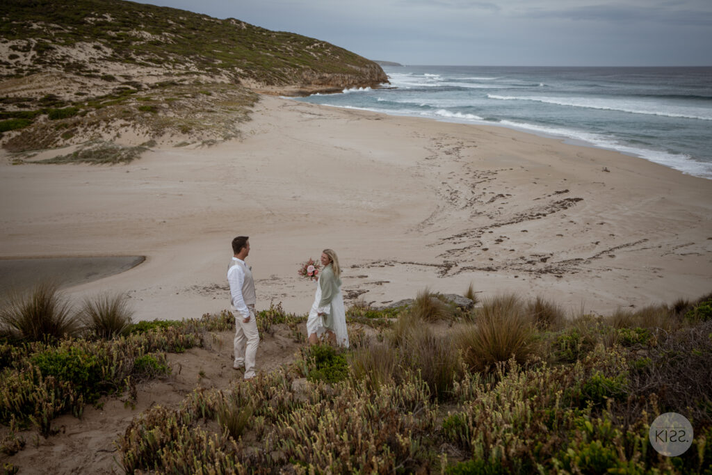 A wedding couple standing above a sandy cove