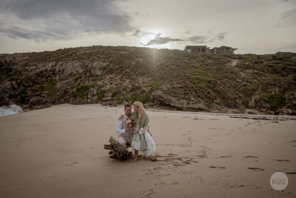 A wedding couple sitting on the sand beneath a cloudy sky