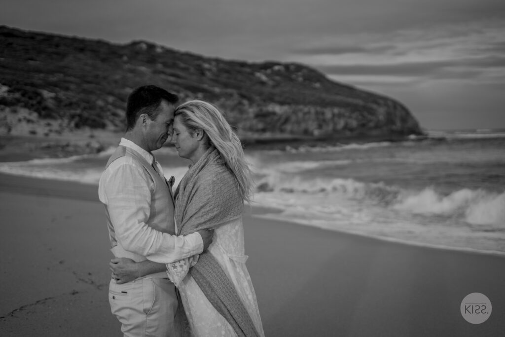 A wedding couple touching foreheads beside the sea in black and white