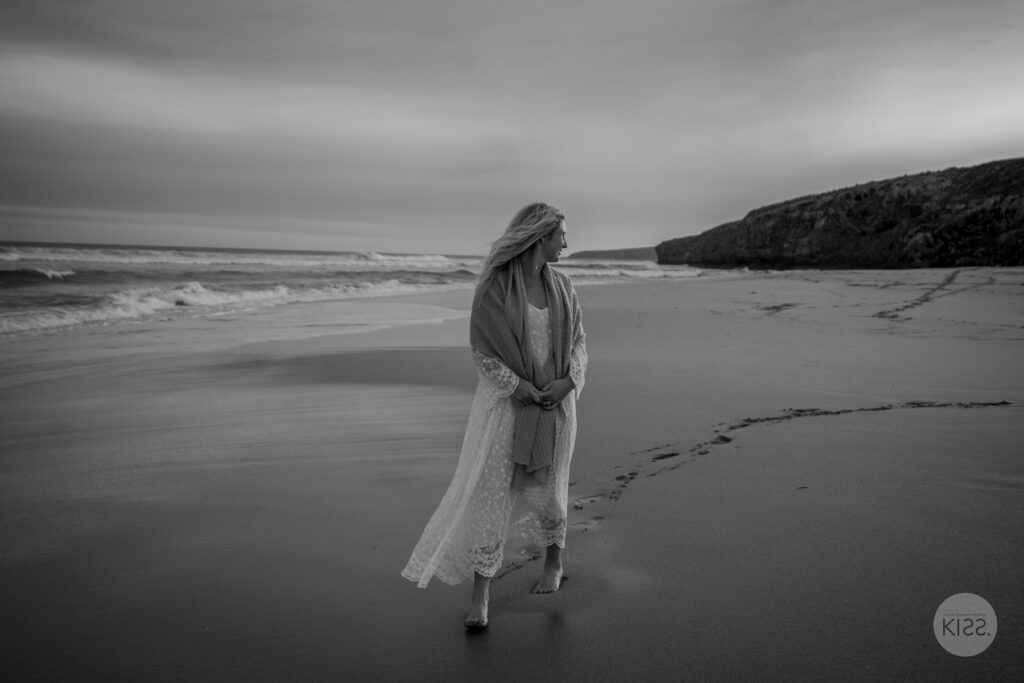 A bride walking along an empty beach in black and white